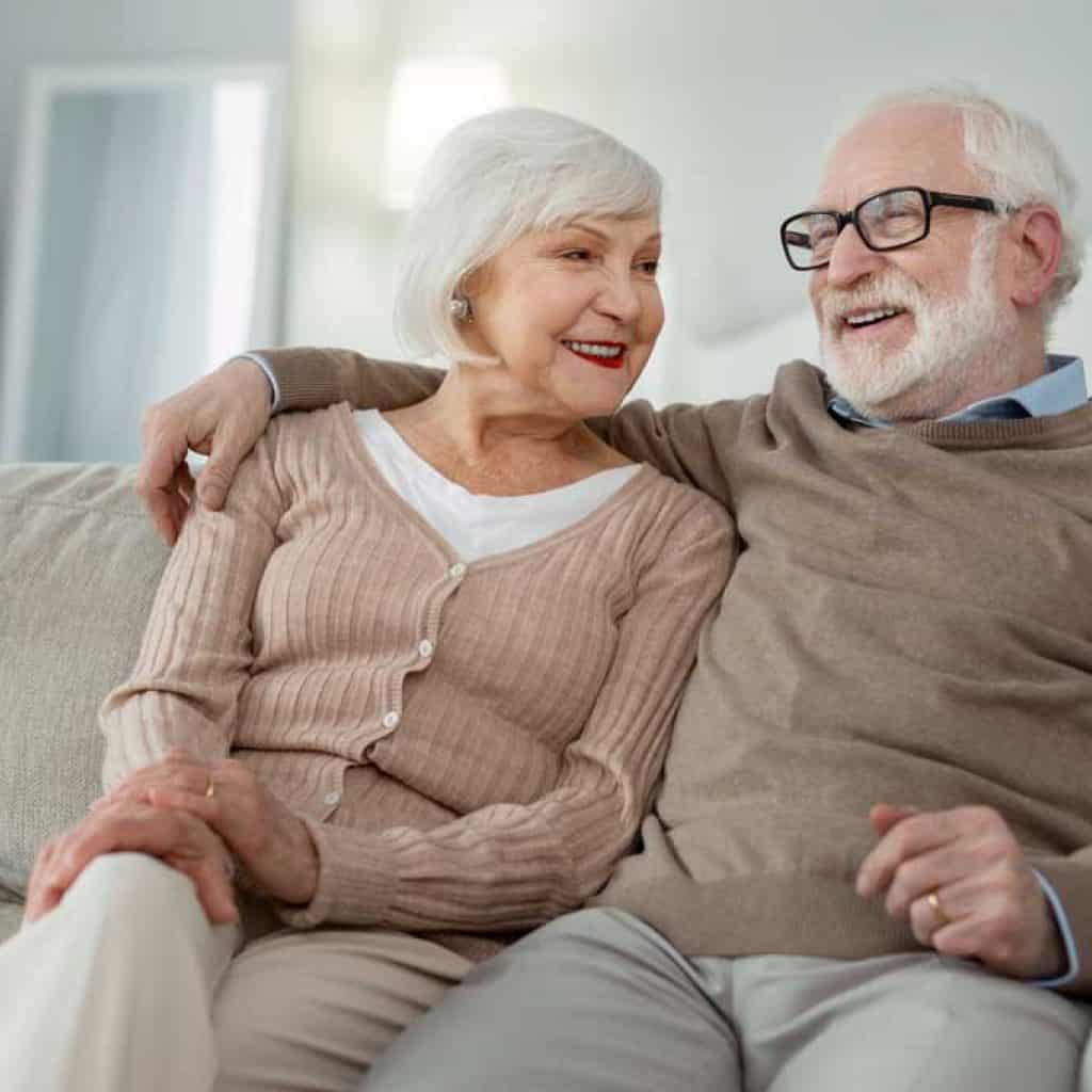 Elderly couple. Joyful aged man hugging his wife while sitting on the sofa