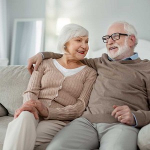 Elderly couple. Joyful aged man hugging his wife while sitting on the sofa