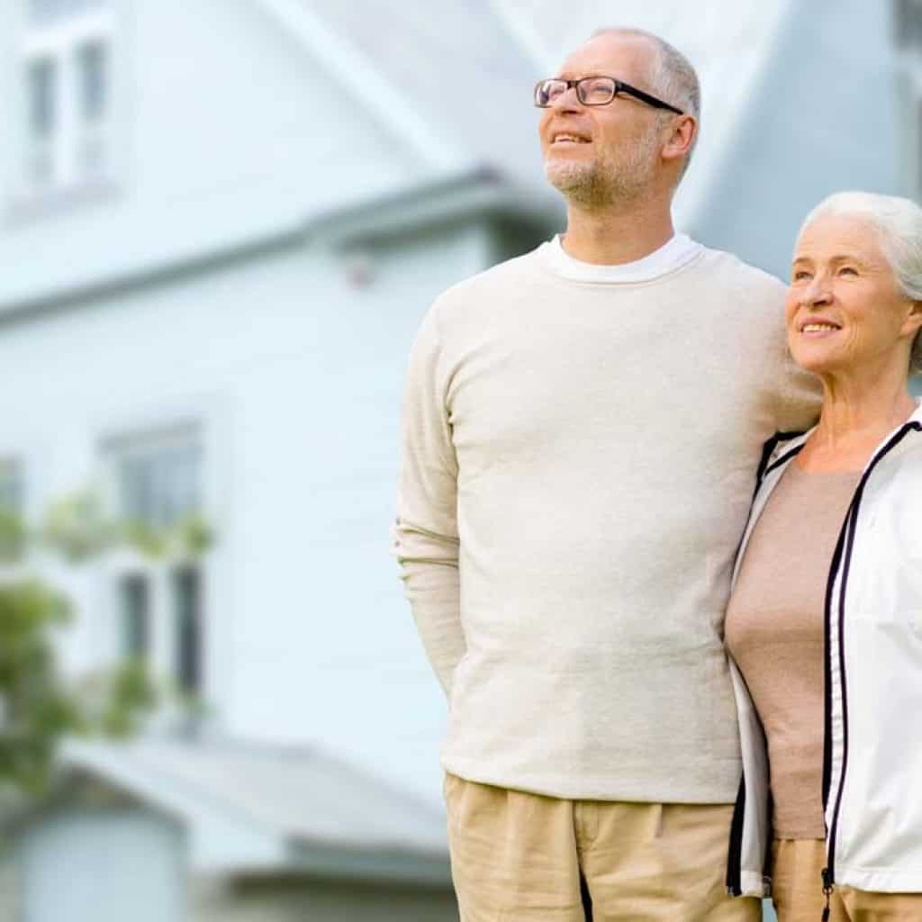 happy senior couple hugging over house background