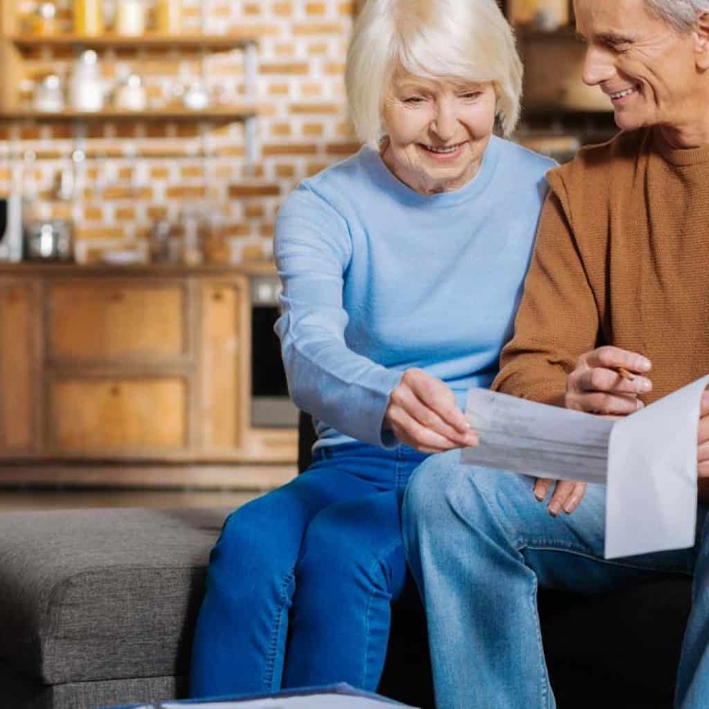 Nice delighted positive couple sitting together and looking at the bills while being happy about them