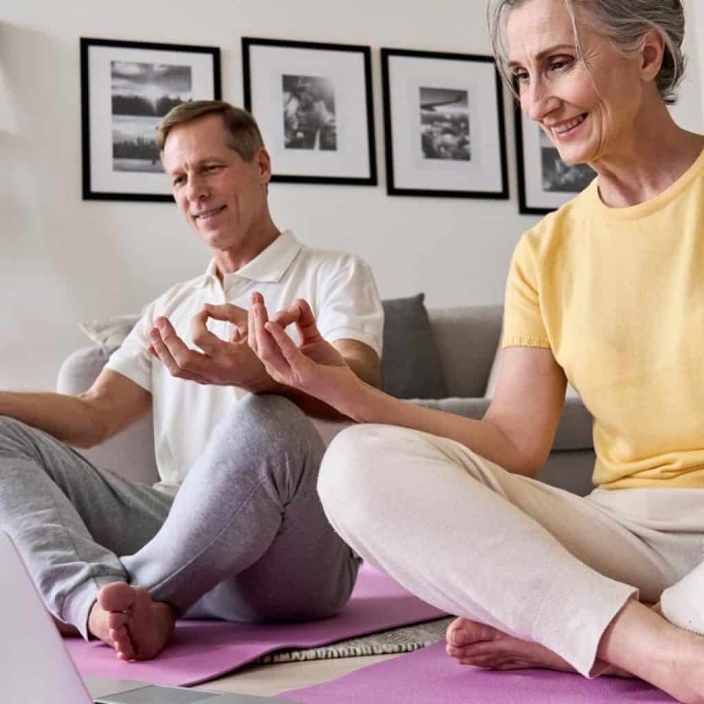 Happy old middle aged senior 50s couple learning to meditate at home