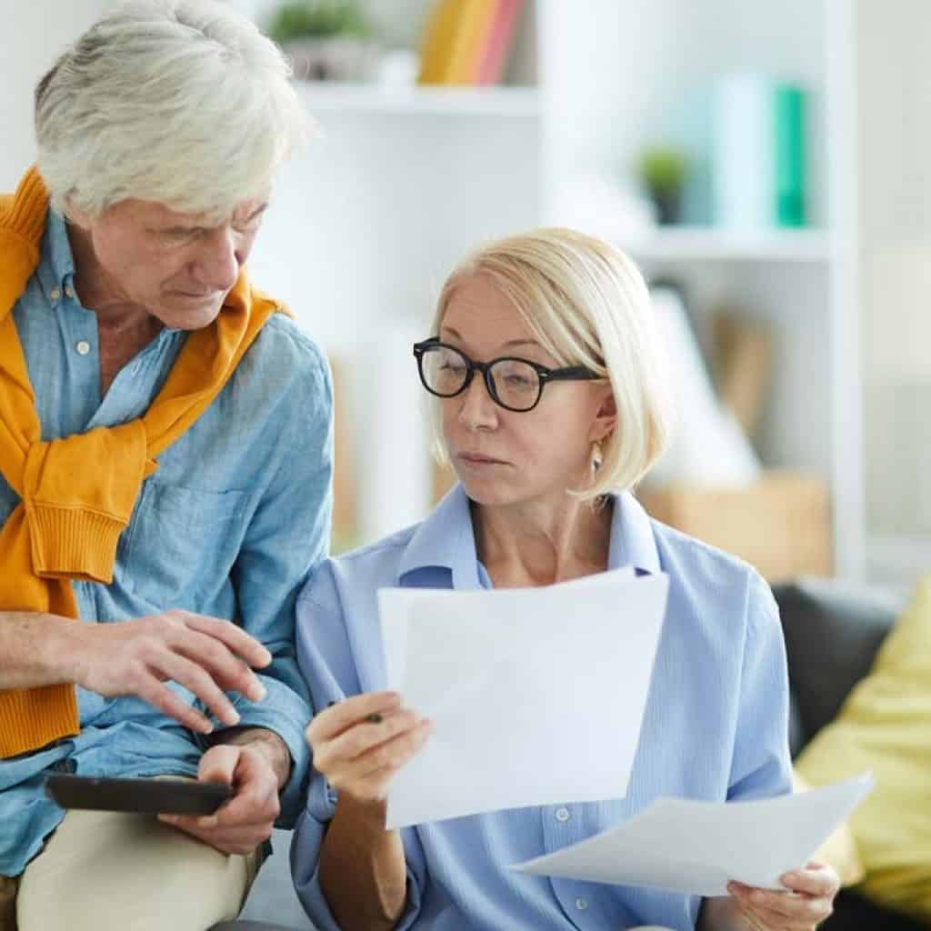 Portrait of contemporary mature couple calculating finances at home holding tax forms, copy space