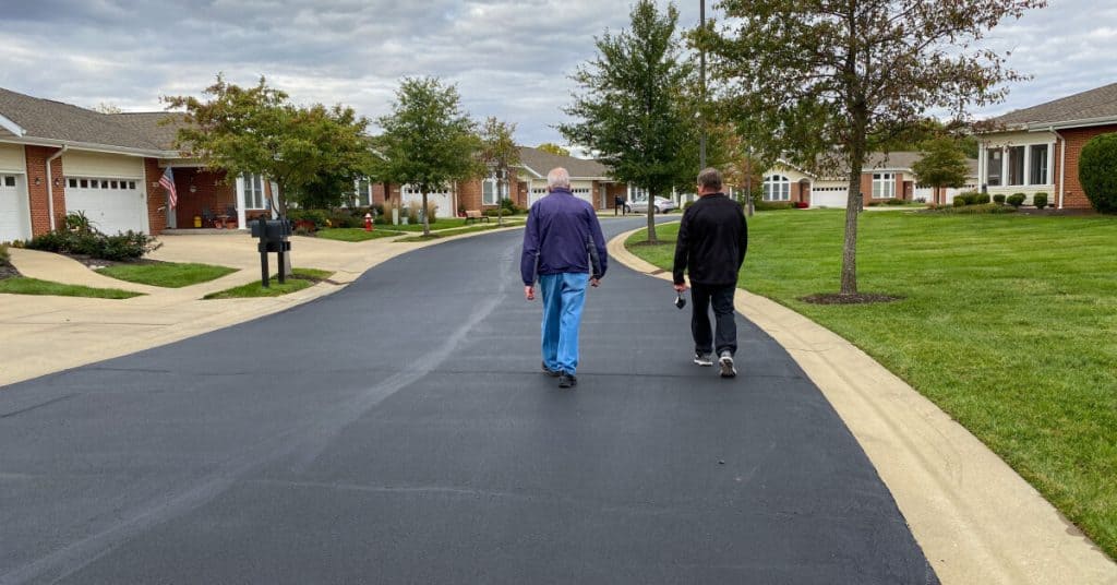 An elderly father and son walking in a senior living facility neighborhood.